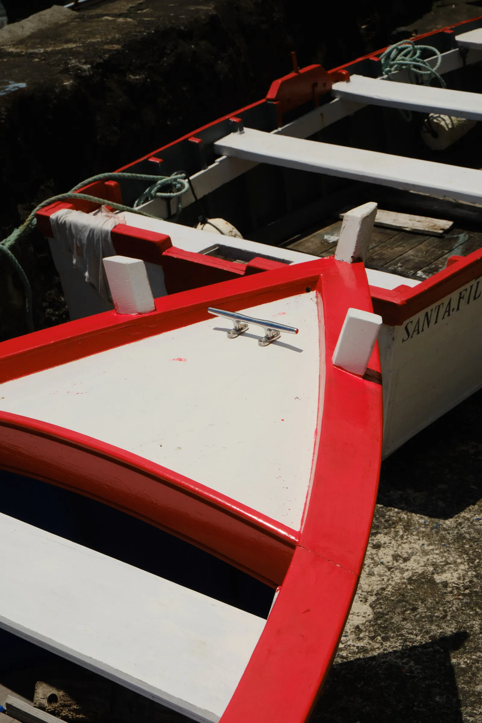 The red and white bow of a small fishing boat, close-up on wet stone.