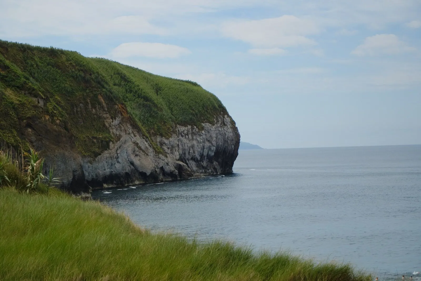 A lush green volcanic headland dropping into the Atlantic.
