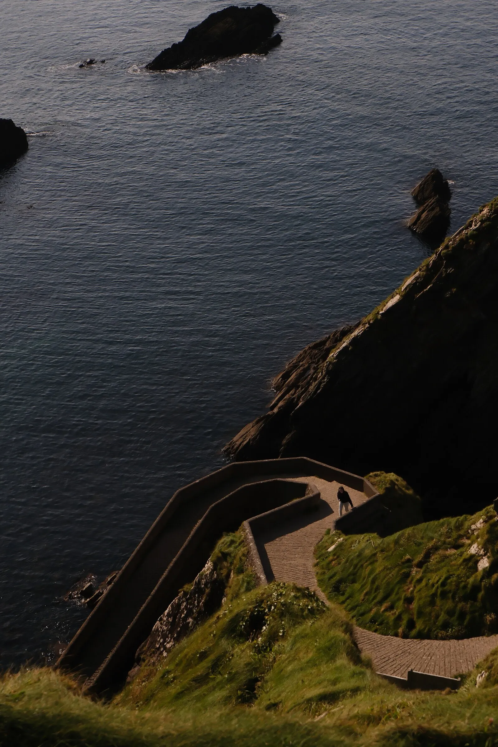 A switchback road descending steep coastal cliffs toward the water, West Cork.