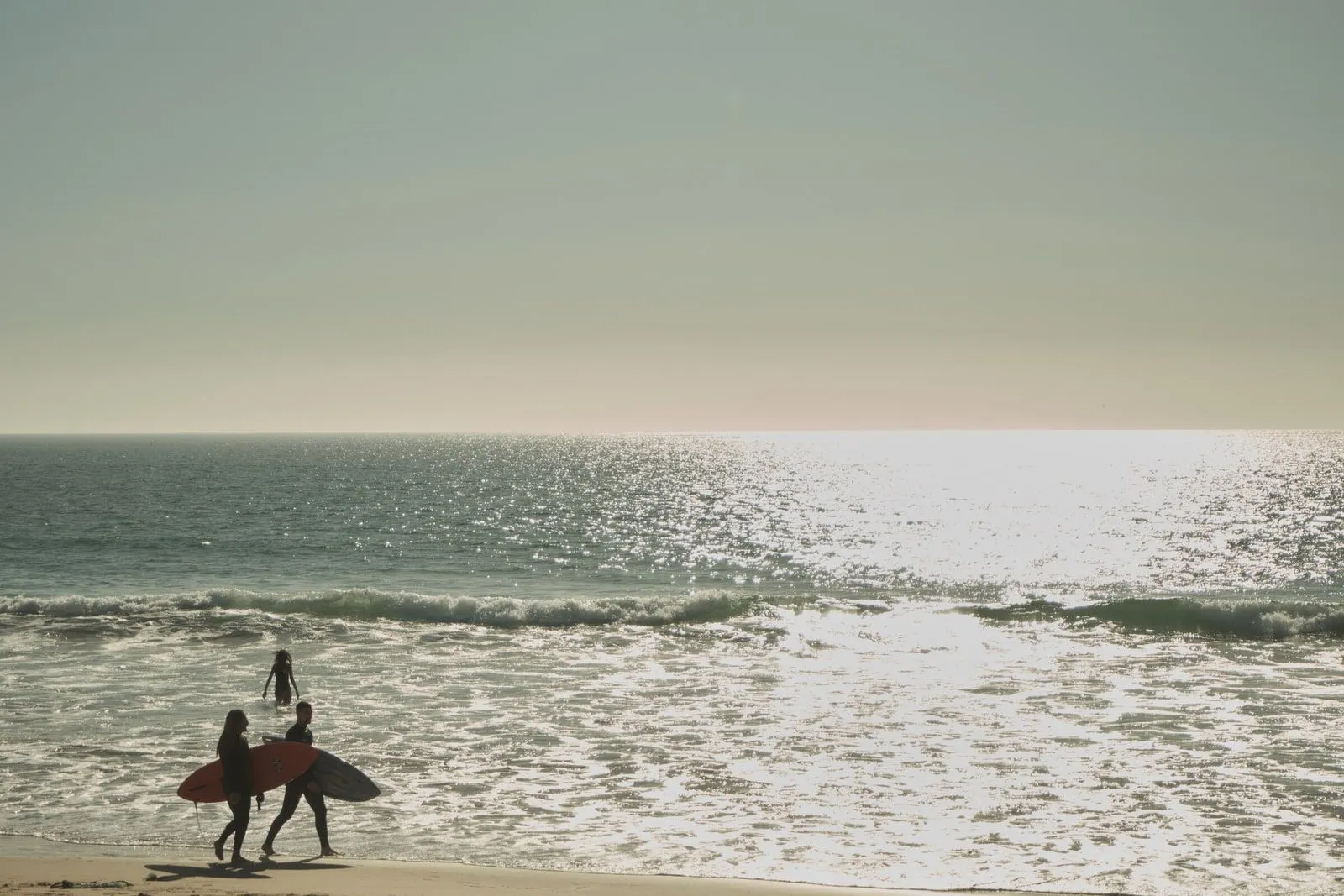 Two surfers walking into overcast, grey-toned surf carrying their boards.