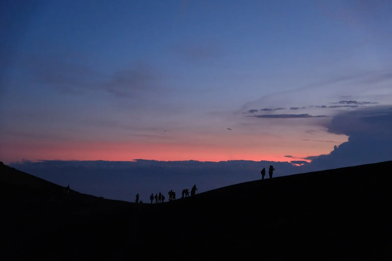 Hikers silhouetted along a high ridge as the sky fades to dusk.